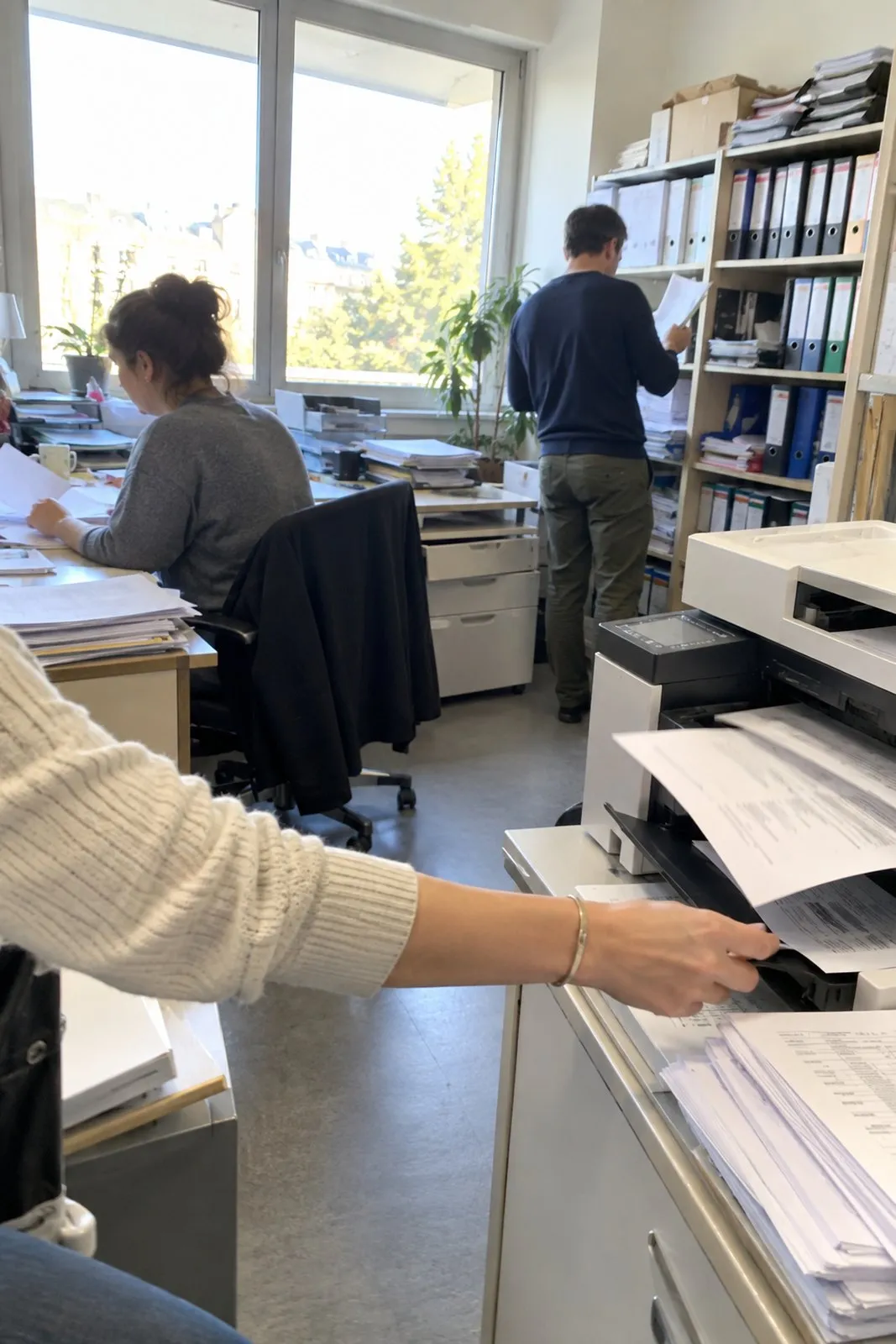 Pisarna računovodskega servisa s kupi map, registratorji in tiskalnikom